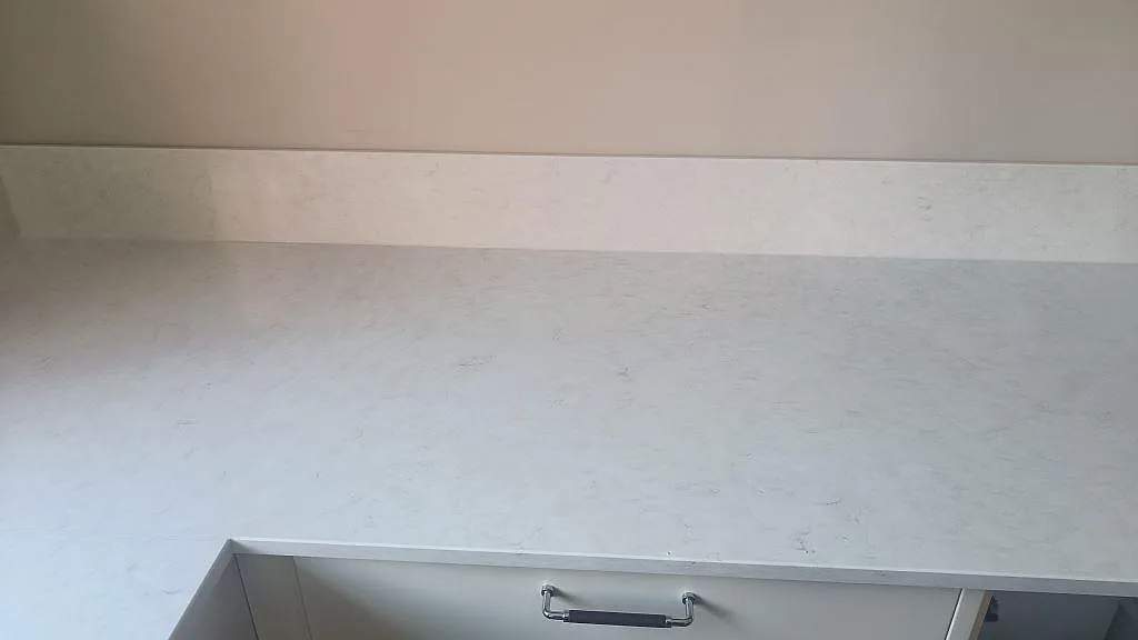 Lång bänkyta i polerad Silestone Snowy Ibiza med ljus ådring och öppna köksstommar i Höllviken.