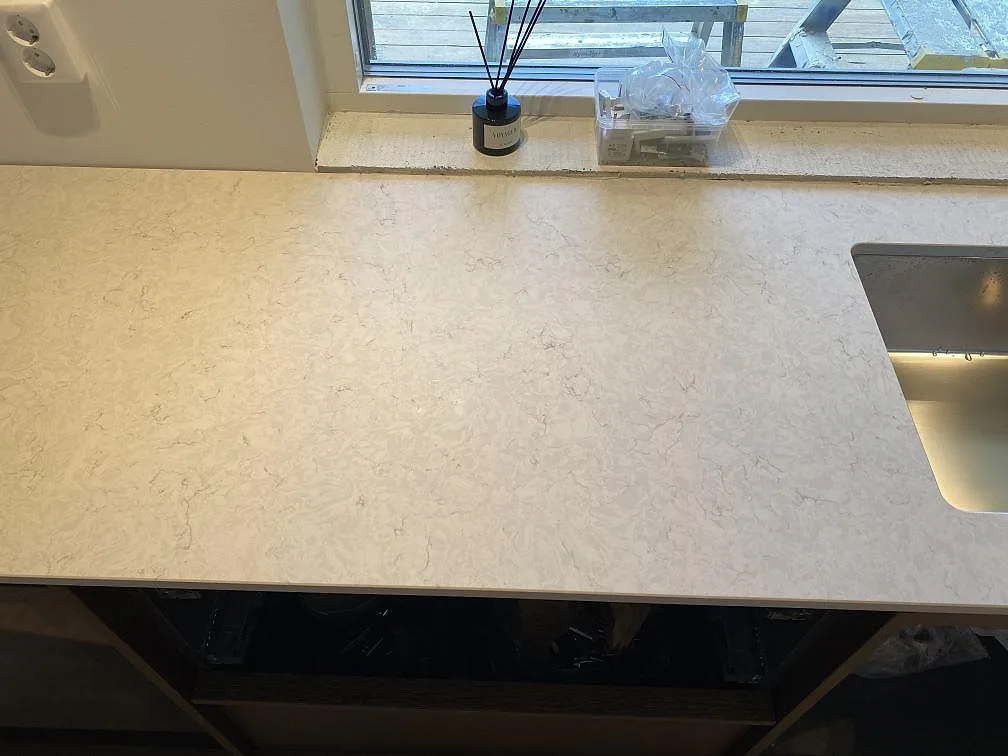Arbetsyta i polerad Silestone Snowy Ibiza vid fönster och diskho, med ljus grå ådring i ett kök i Höllviken.