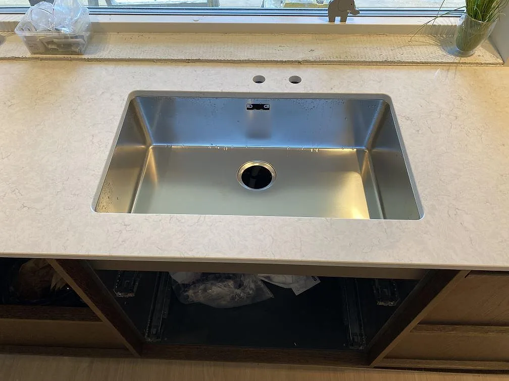 Underlimmad rostfri diskho i en polerad köksbänkskiva av Silestone Snowy Ibiza med borrade hål för blandare i ett kök i Höllviken.