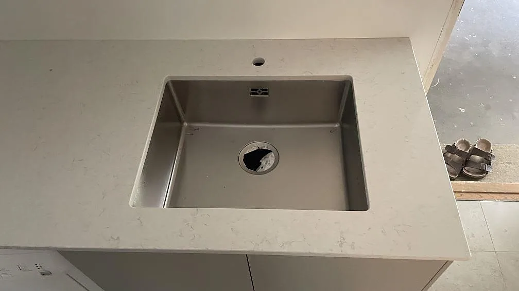 Närbild av polerad Silestone Snowy Ibiza i kvartskomposit runt en rostfri diskho och ett blandarhål i Höllviken.