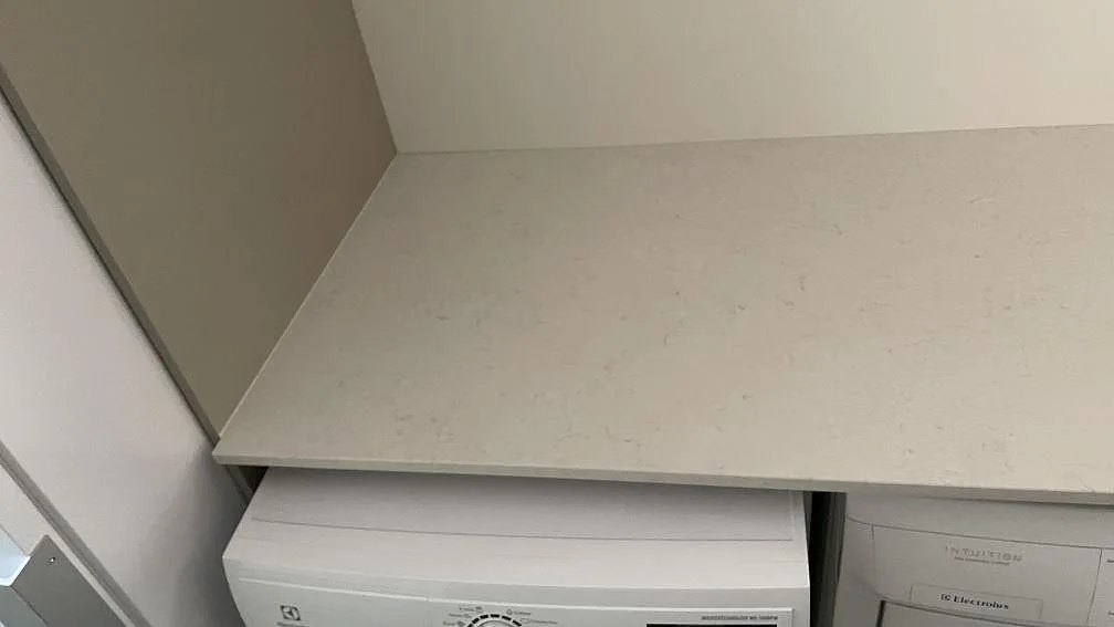 Detalj av den polerade Silestone Snowy Ibiza-skivan över vitvaror i en tvättstuga i Höllviken, med diskret grå ådring.