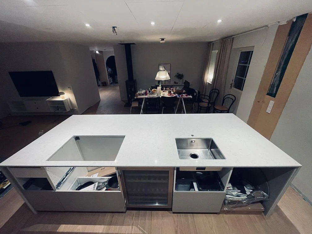 Vit Silestone Snowy Ibiza köksö med urtag för underlimmad rostfri diskho och infälld induktionshäll samt integrerad vinkyl, fotat under montering i Höllviken.