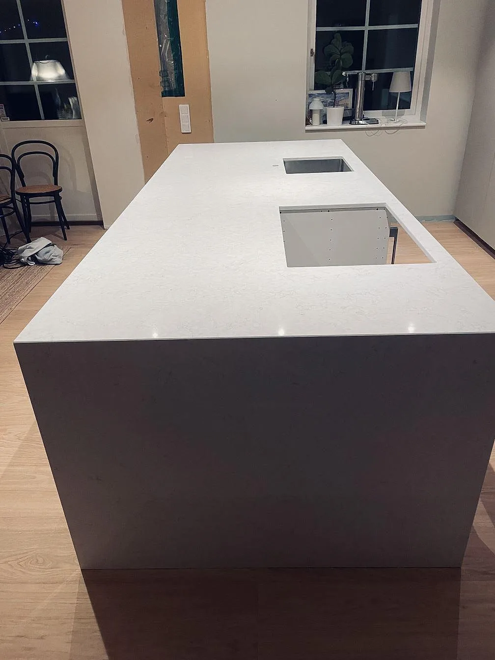 Polerad Silestone Snowy Ibiza bänkskiva på köksö sedd mot fönster, med underlimmad rostfri diskho och urtag för häll i ett kök i Höllviken.