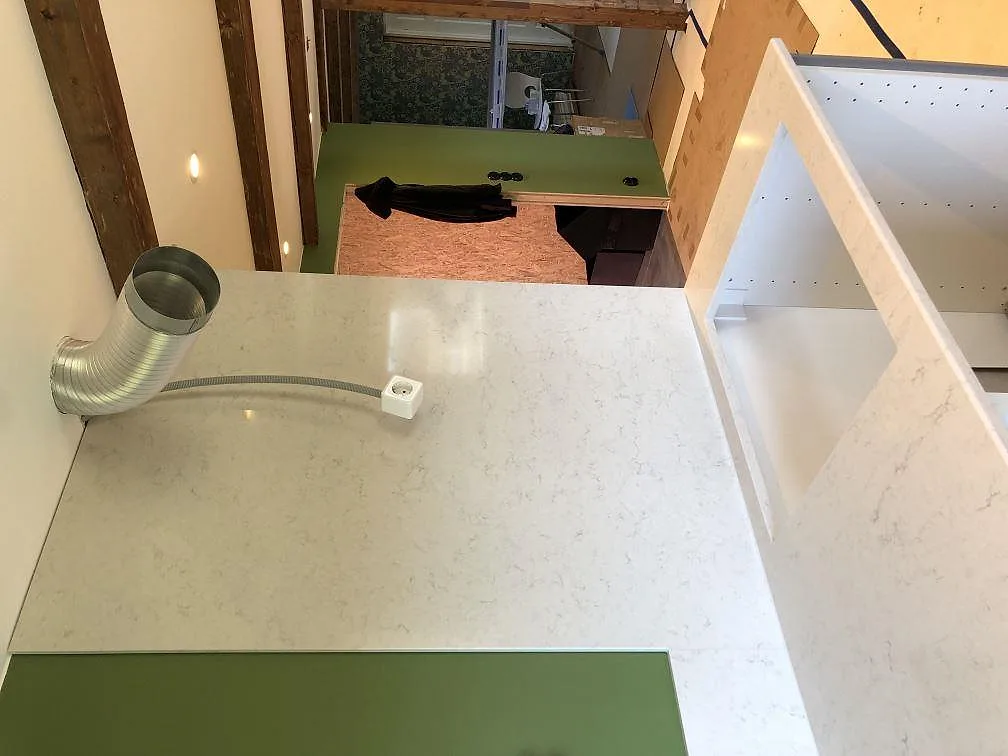 Vinklad köksbänkskiva i vit Silestone Snowy Ibiza med uppvikt stänkkant mot grön vägg i ett kök i Hörby.
