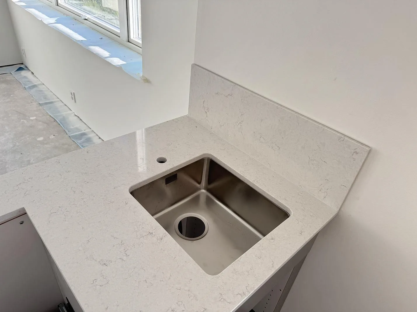 Diskhozonen med polerad Silestone Snowy Ibiza, rostfri diskho och låg stänkkant under ett fönster i Holm.