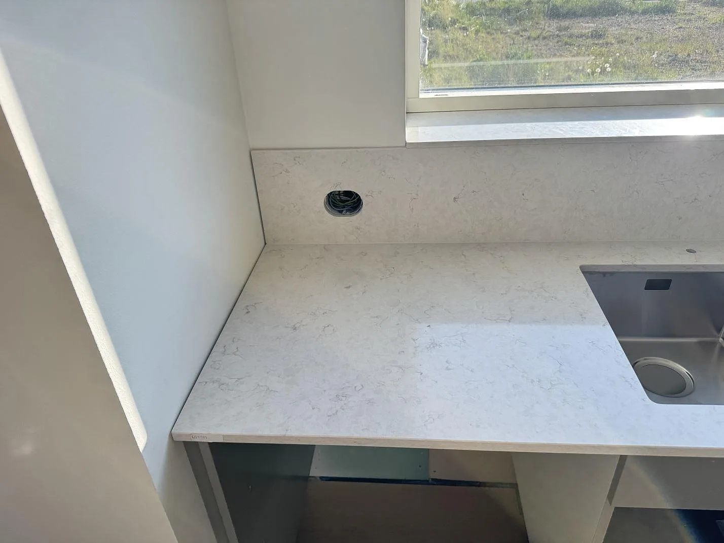 Rak bänkyta i polerad Silestone Snowy Ibiza vid fönster och diskho, med ljus kvartskomposit i ett kök i Holm.