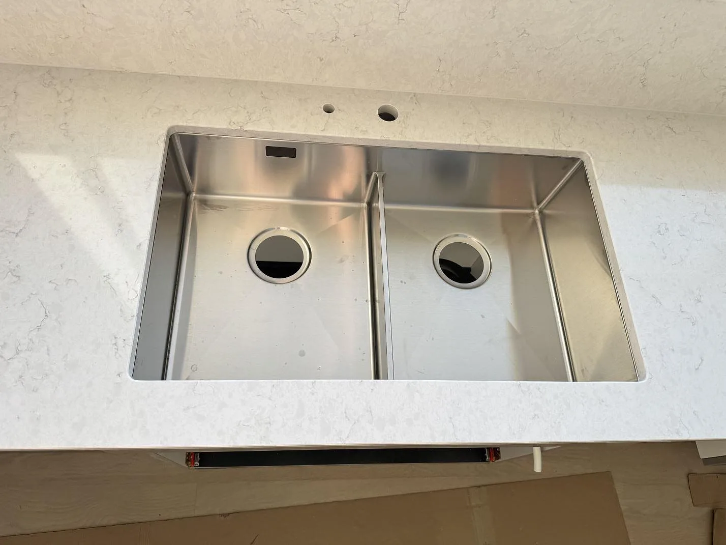 Närbild på rostfri dubbelho i en polerad Silestone Snowy Ibiza bänkskiva med ljus grå teckning i ett kök i Holm.