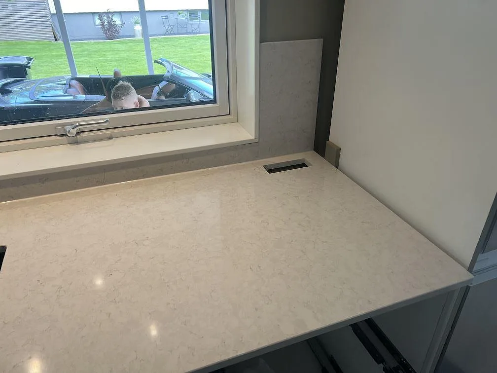 Polerad arbetsyta i Silestone Snowy Ibiza komposit under fönster, med ljus ådring och stänkskydd i ett kök i Hovmantorp.