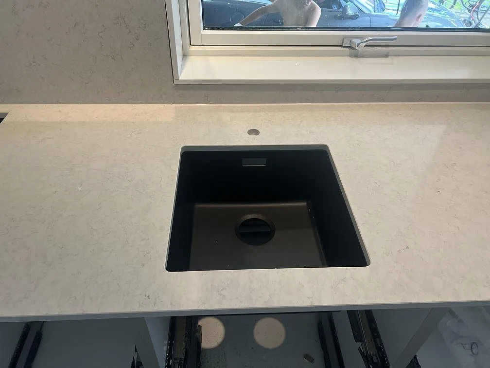 Närbild på polerad Silestone Snowy Ibiza komposit med svart diskho och ljus ådring i ett kök under montering i Hovmantorp.