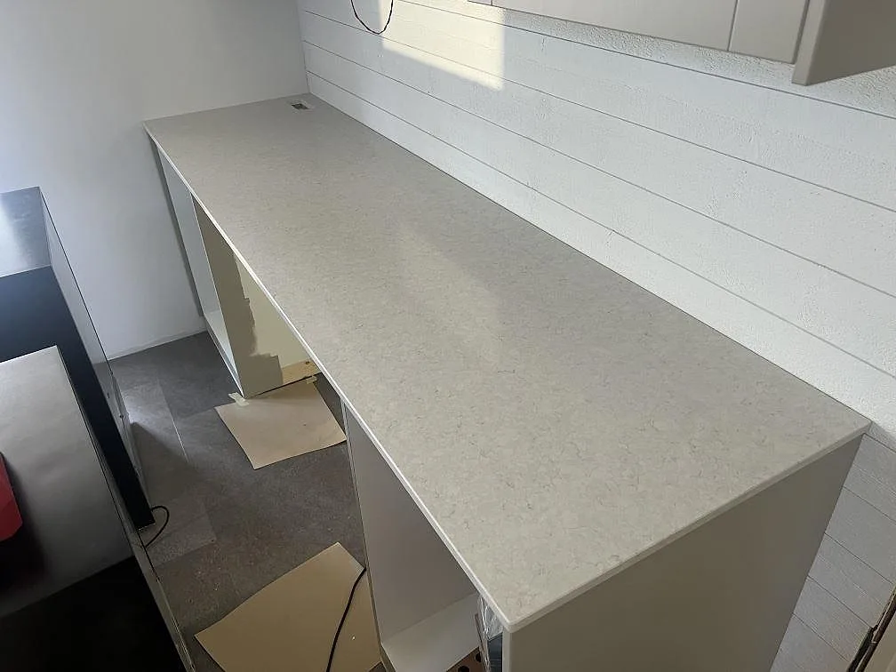 Lång köksbänk i polerad Silestone Snowy Ibiza komposit längs vit vägg, fotograferad under montering i Hovmantorp.