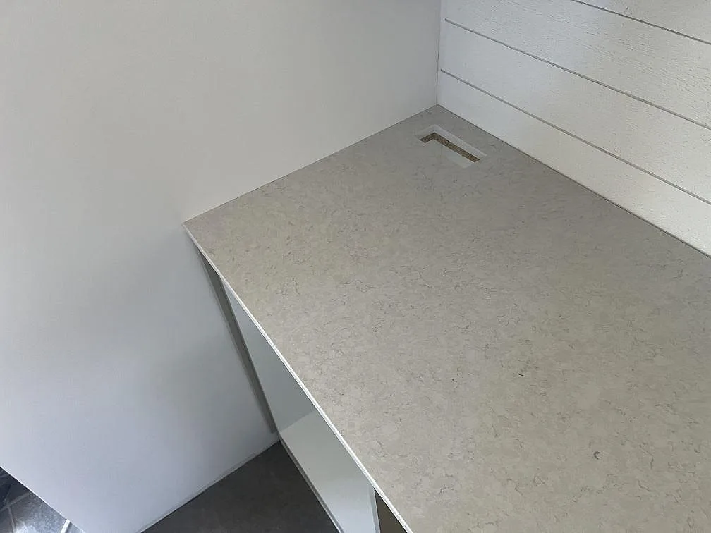 Ändparti av polerad köksbänkskiva i Silestone Snowy Ibiza komposit med diskret ådring och urtag vid väggen i Hovmantorp.