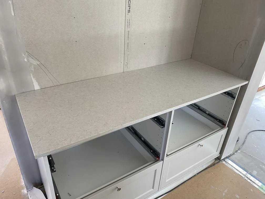 Rak sidobänk i polerad Silestone Snowy Ibiza på vita köksstommar under montering i Hunnebostrand.