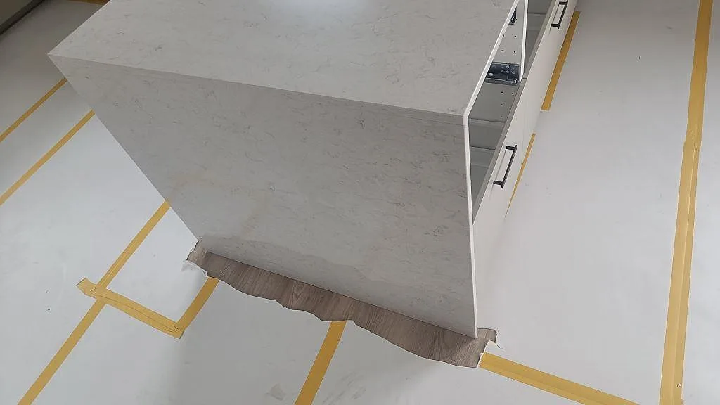 Detalj av vattenfallsida på köksö i polerad Silestone Snowy Ibiza med skyddstejp på golvet i Huskvarna.