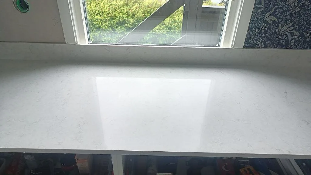 Rak bänkskiva i polerad Silestone Snowy Ibiza med reflektion från stort fönster och öppna köksstommar i Huskvarna.