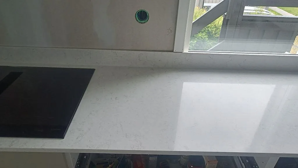 Polerad Silestone Snowy Ibiza som köksbänkskiva med svart häll och stenkant vid fönster i ett kök i Huskvarna.