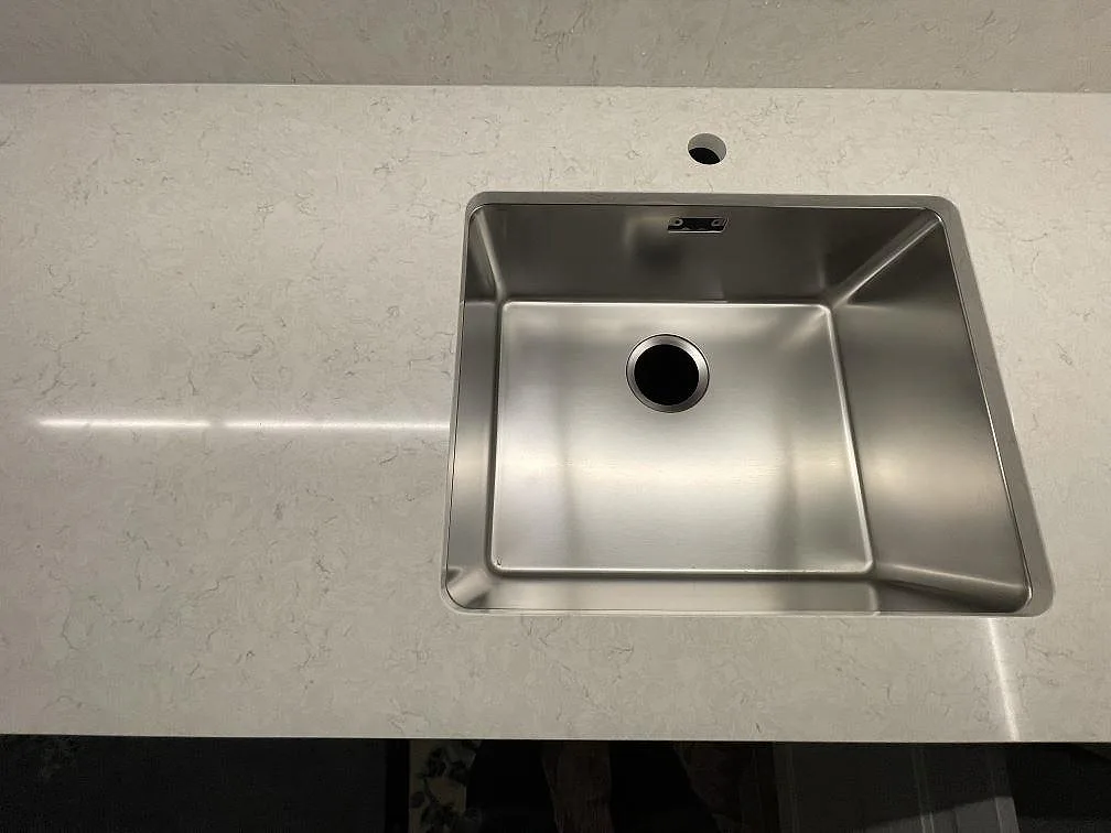 Polerad köksbänkskiva i Silestone Snowy Ibiza med en stor underlimmad rostfri diskho och kranhål i ett kök i Järfälla.