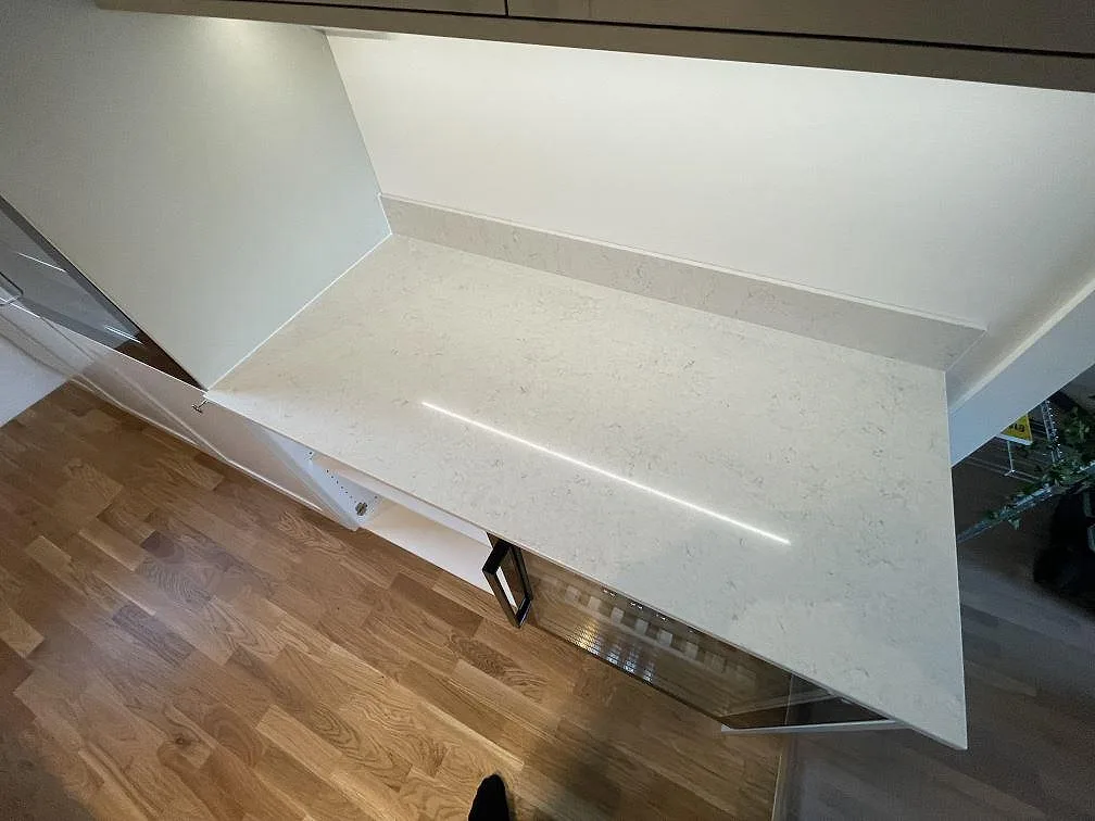 Polerad bänkskiva i Silestone Snowy Ibiza med mjuk grå ådring och nedåtdragen gavel sedd snett uppifrån i ett kök i Järfälla.