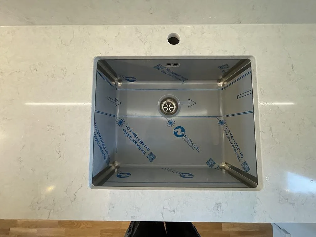 Underlimmad rostfri diskho med borrat blandarhål i en köksbänkskiva av Silestone Snowy Ibiza i Järfälla.