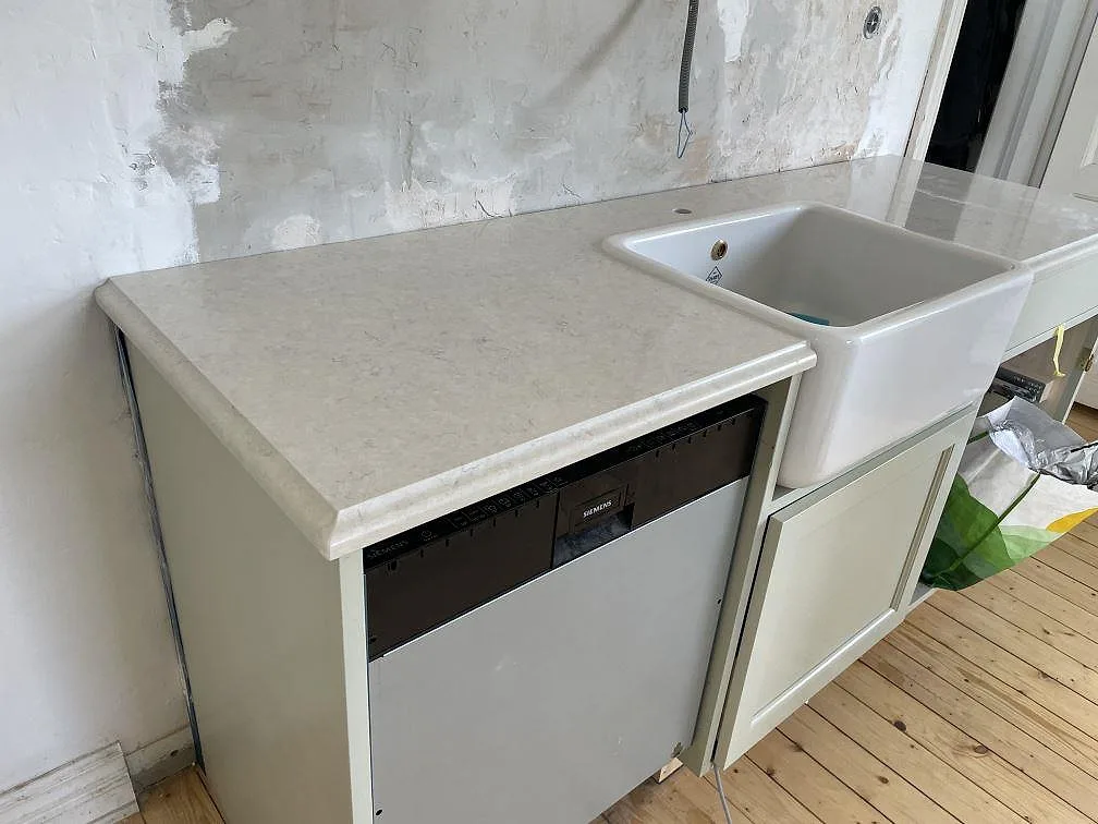 Polerad Silestone Snowy Ibiza som köksbänkskiva runt en vit frontsynlig diskho och diskmaskin i Kågeröd.