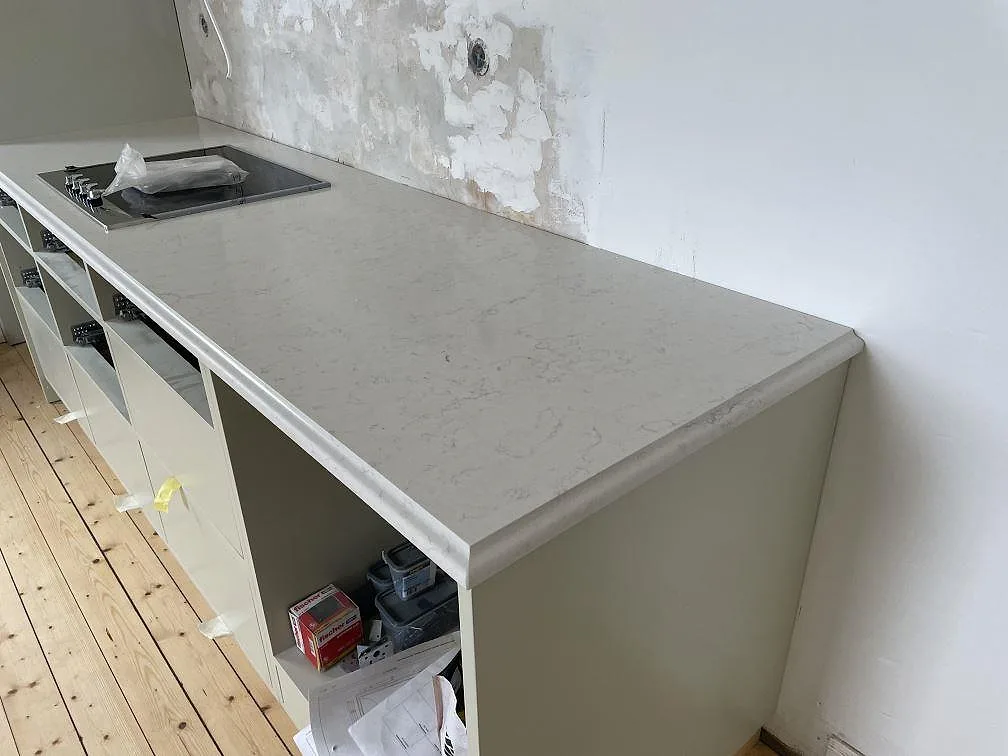 Lång köksbänkskiva i Silestone Snowy Ibiza, polerad komposit, med svart häll och ljusa stommar i Kågeröd.