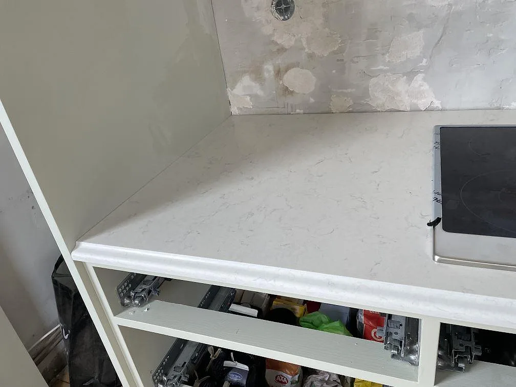 Detaljbild av arbetsyta i polerad Silestone Snowy Ibiza intill svart häll och öppna köksstommar i Kågeröd.