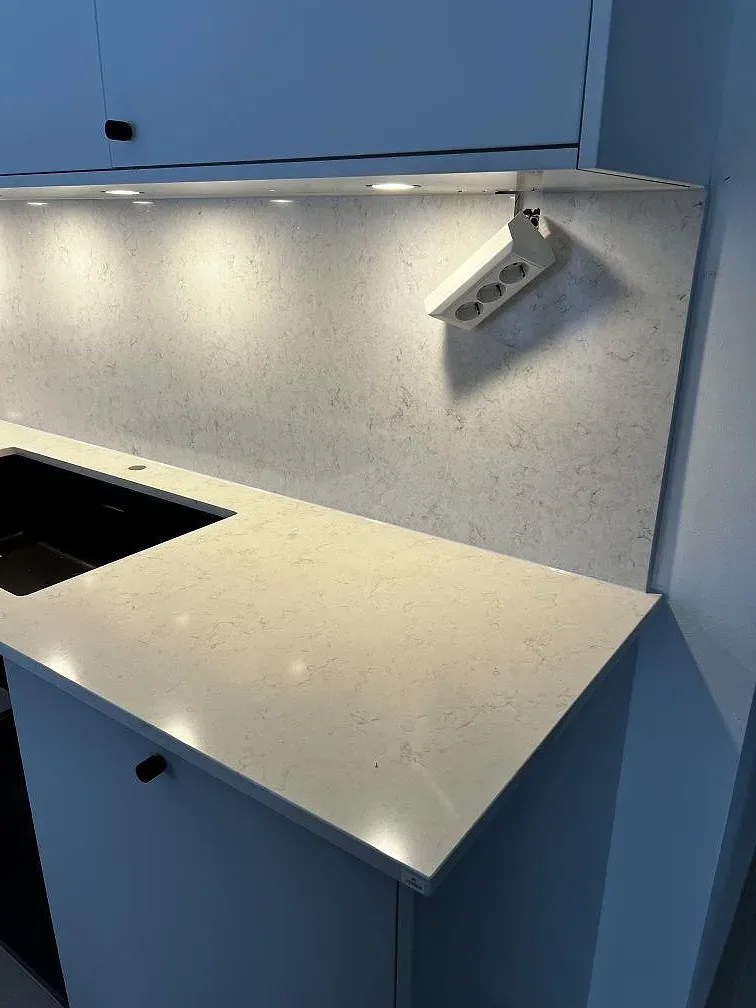 Polerad Silestone Snowy Ibiza som ljus köksbänk och väggbeklädnad med infällda spotlights och mörk ho i Kalmar.
