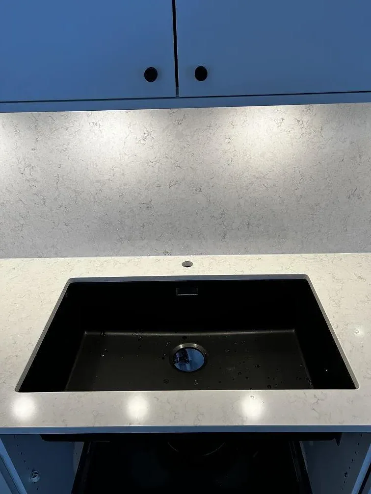 Närbild på köksbänkskiva i polerad Silestone Snowy Ibiza med mörk ho, blandarhål och belyst väggskiva i ett kök i Kalmar.