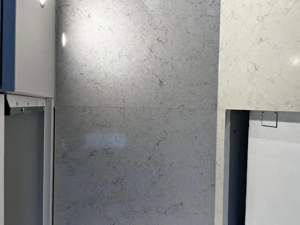 Väggdel i polerad Silestone Snowy Ibiza, 12 mm, med matchande bänkskiva och belyst stenytan i ett kök i Kalmar.