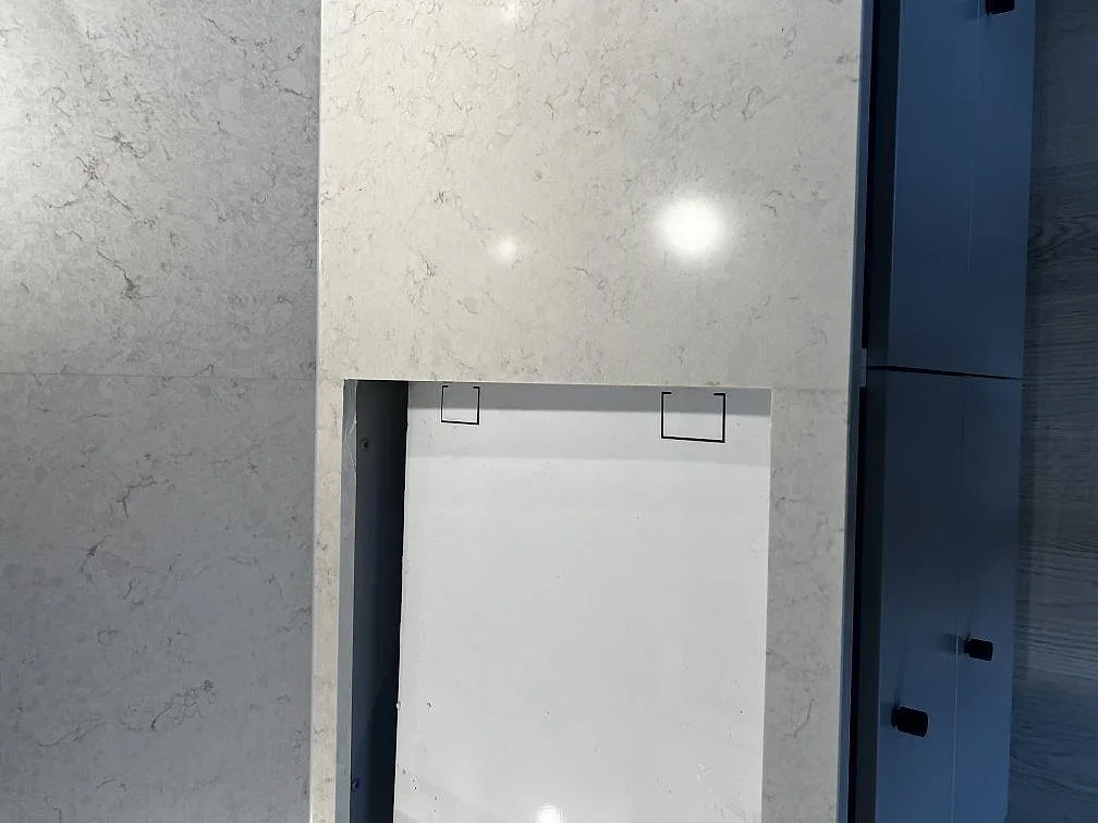 Köksnisch med polerad Silestone Snowy Ibiza runt öppningen, ljus kompositsten och mörka stommar i Kalmar.