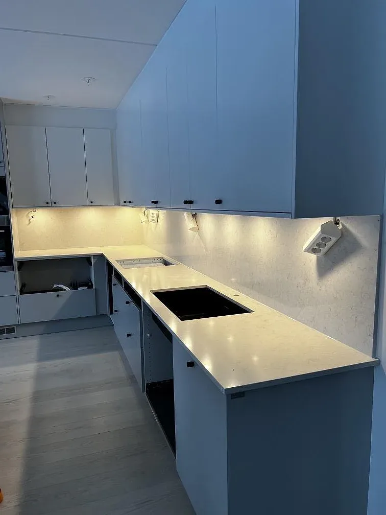 Köksbänkskiva i polerad Silestone Snowy Ibiza, 20 mm, med häll, mörk ho och stenklädd vägg i ett kök under montering i Kalmar.