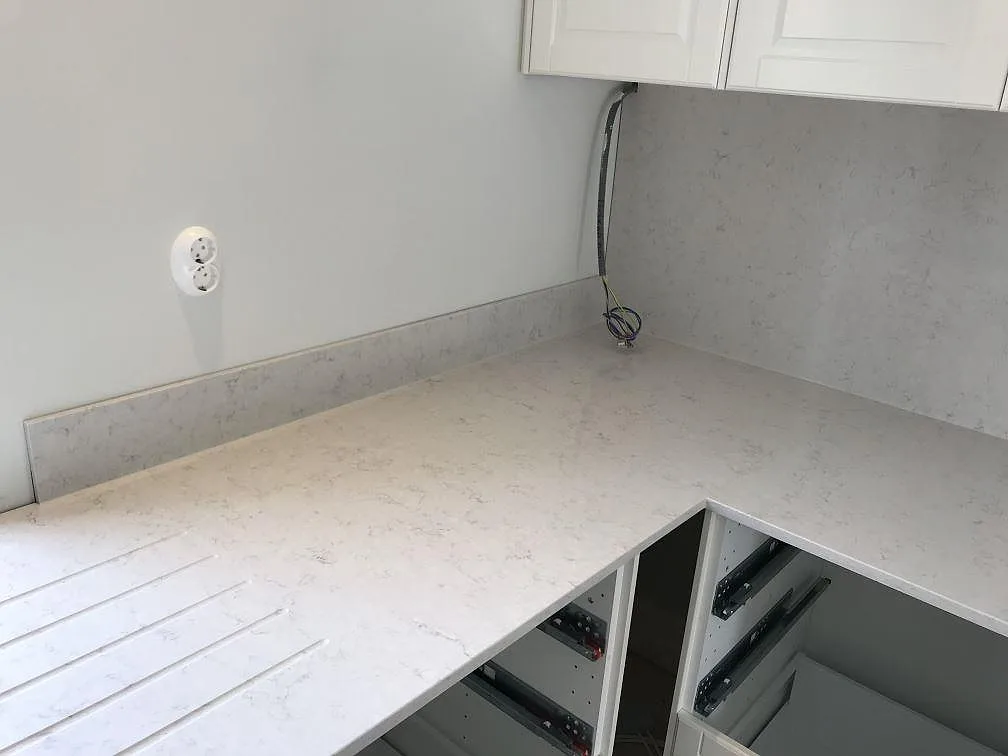 Ovanifrån av L-formad köksbänkskiva i polerad Silestone Snowy Ibiza med avrinningsspår och fin grå ådring i ett kök i Karlshamn.