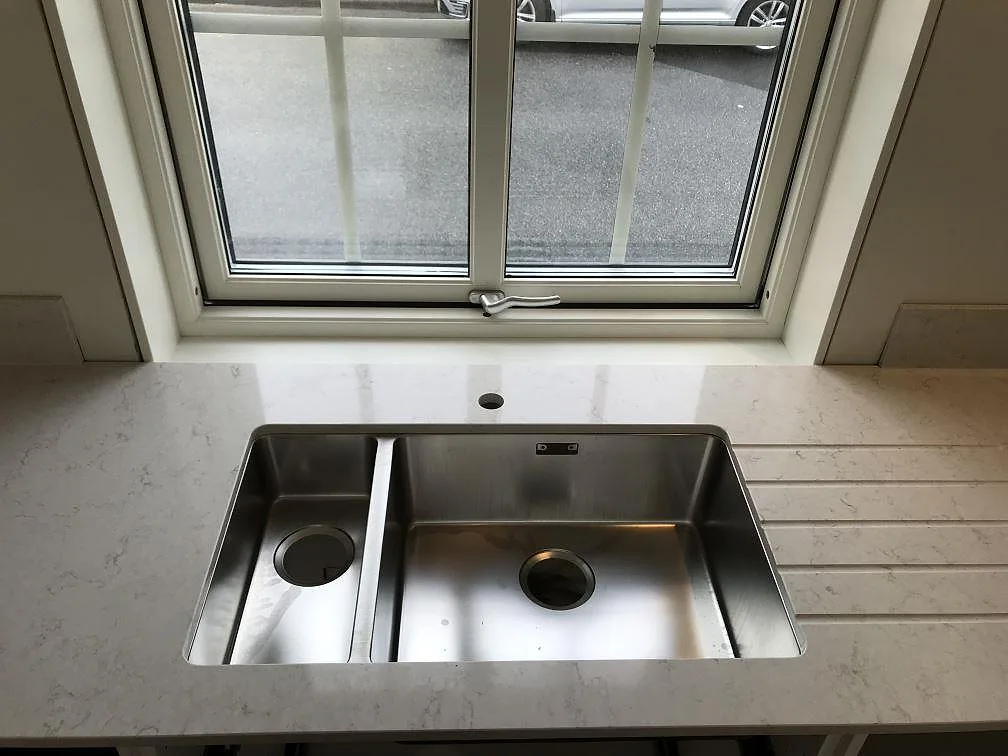 Underlimmad rostfri diskho i polerad köksbänkskiva av Silestone Snowy Ibiza under köksfönstret i Karlshamn.