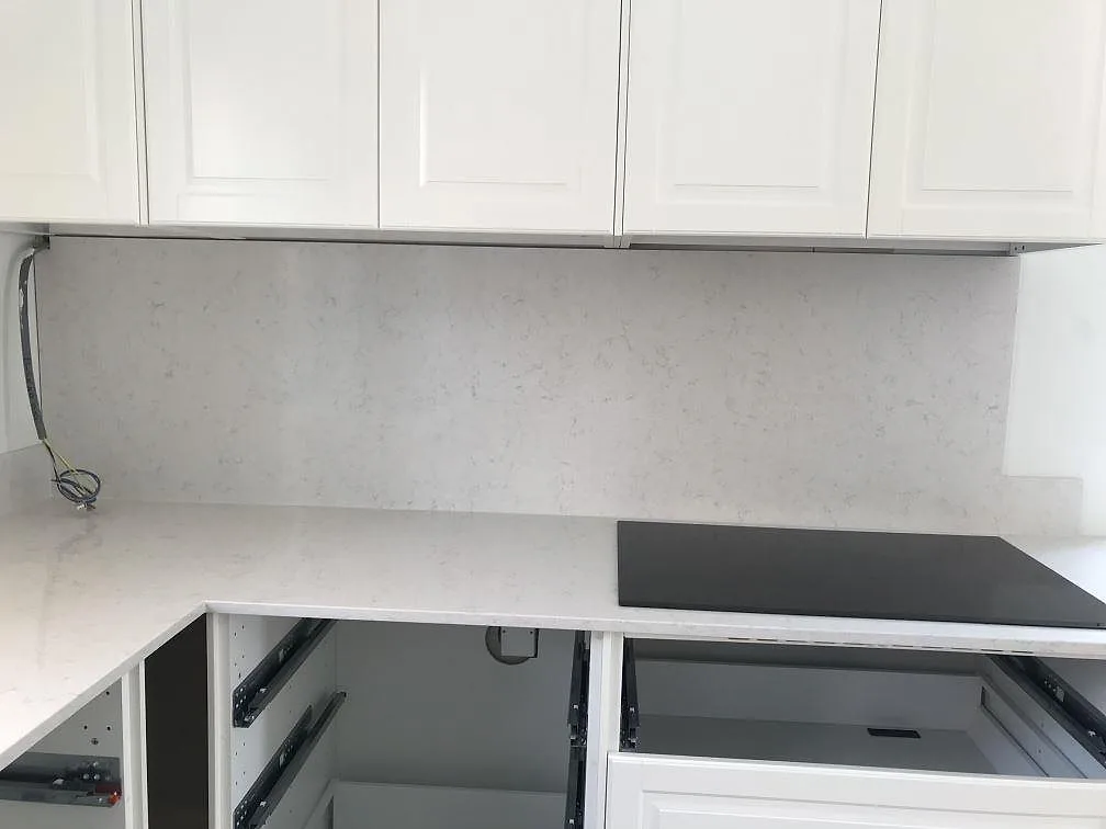 Köksbänkskiva i Silestone Snowy Ibiza med uppvikt stänkkant och infälld induktionshäll under montering i ett kök i Karlshamn.