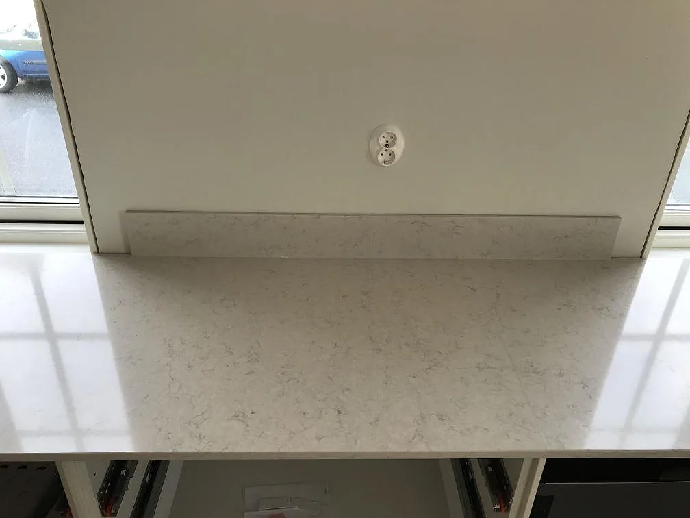 Detalj av polerad Silestone Snowy Ibiza med låg uppvikt stänkkant och eluttag i ett kök i Karlshamn.