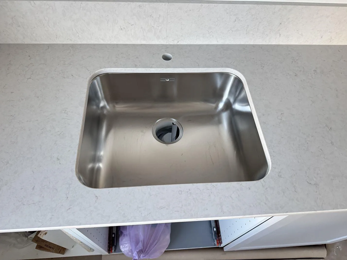 Närbild på rostfri diskho monterad i en polerad Silestone Snowy Ibiza bänkskiva med matchande stänkkant i Karlshamn.