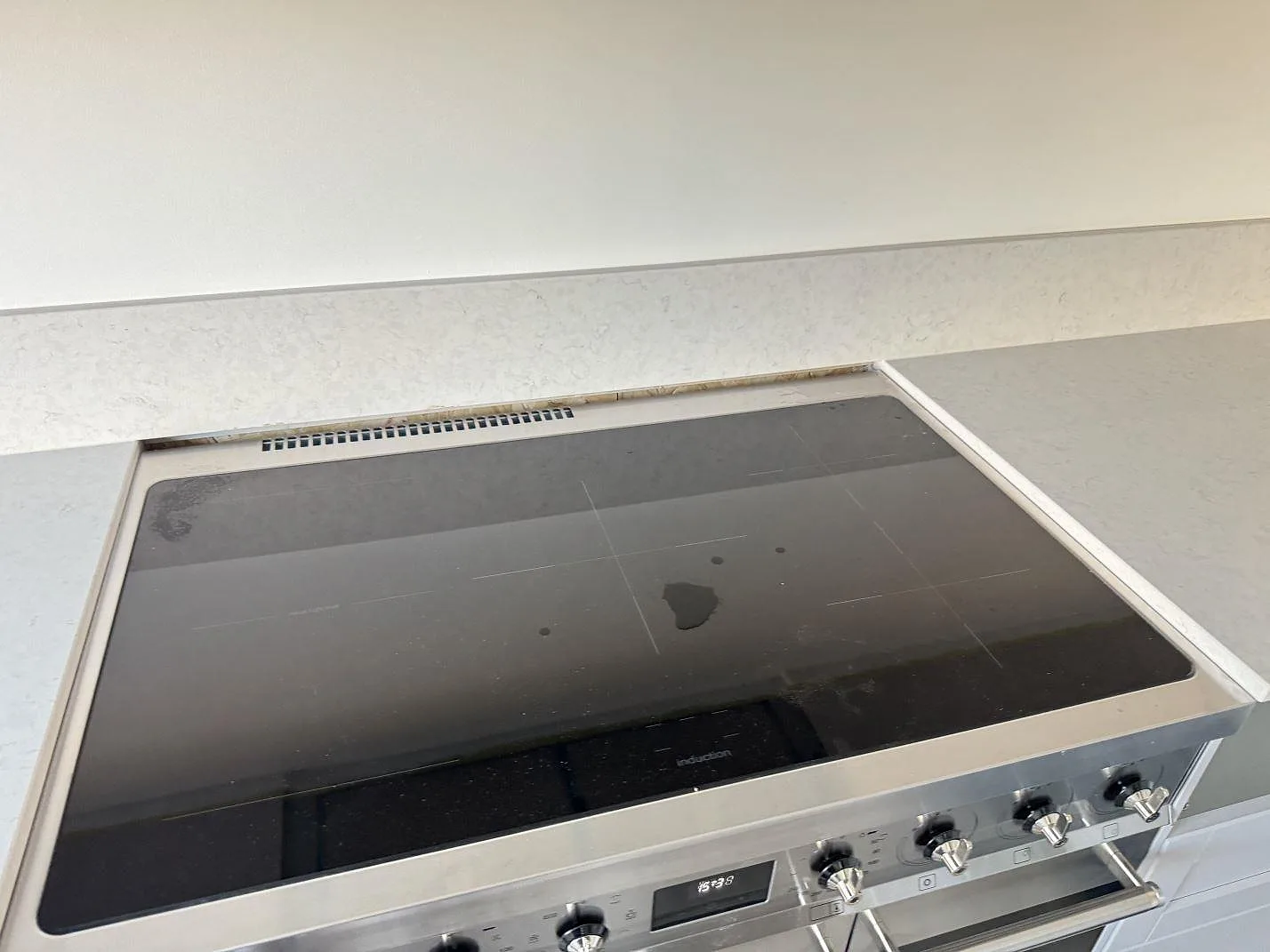 Detalj av spis och polerad Silestone Snowy Ibiza bänkskiva med matchande stänkkant i Karlshamn.