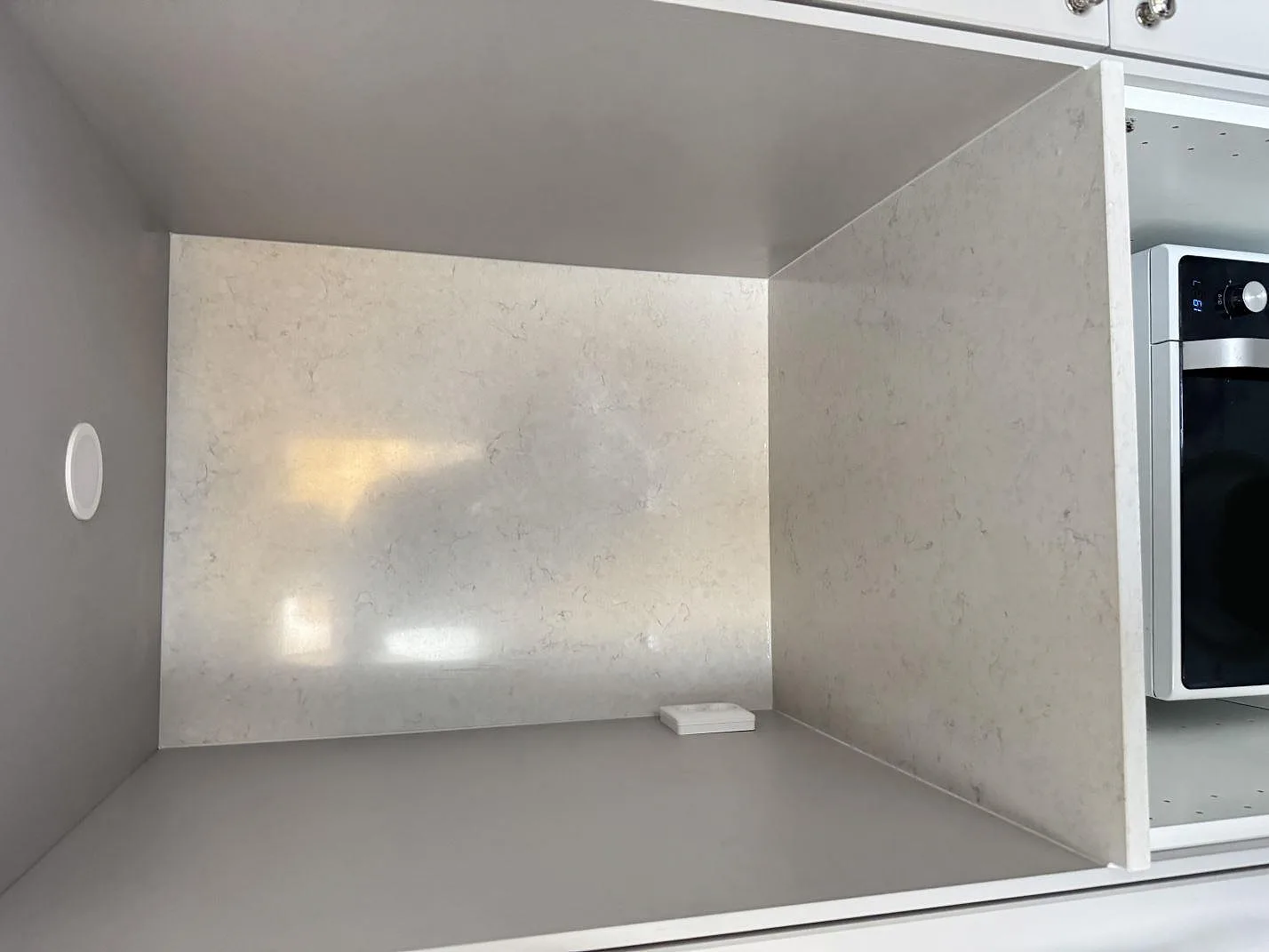 Ljus polerad Silestone Snowy Ibiza på vertikala väggytor i en köksnisch med synlig kompositådring i Karlshamn.