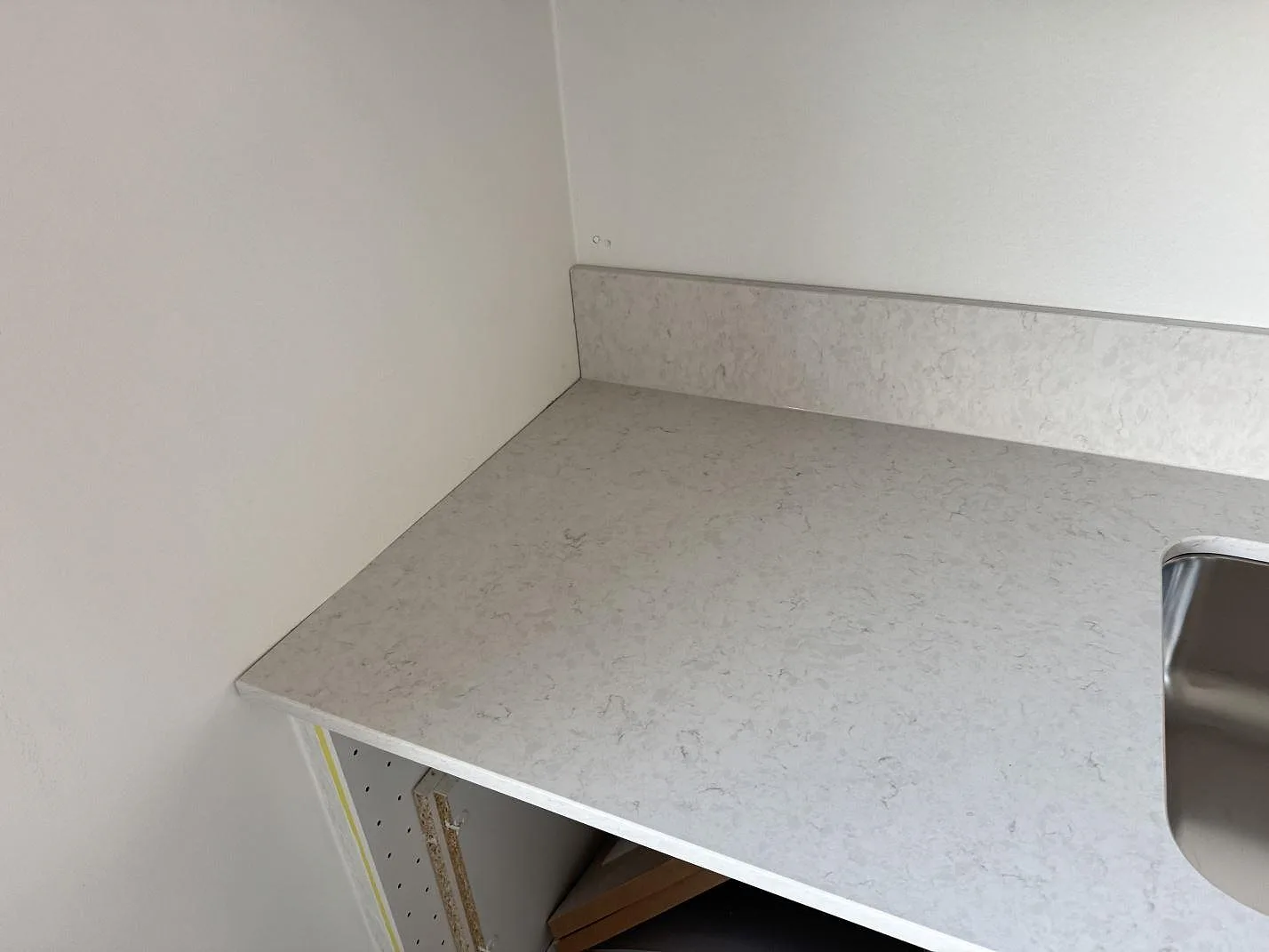 Polerad kompositbänkskiva i Silestone Snowy Ibiza med ljus ådring, låg stänkkant och diskho vid vägg i Karlshamn.