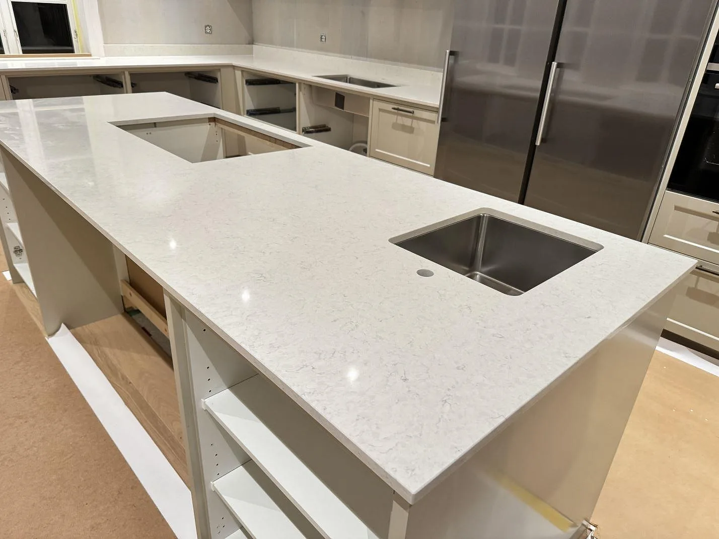 Polerad köksö i Silestone Snowy Ibiza med underlimmad rostfri diskho och borrat blandarhål, sedd mot stommarna i ett U-kök i Karlshamn.
