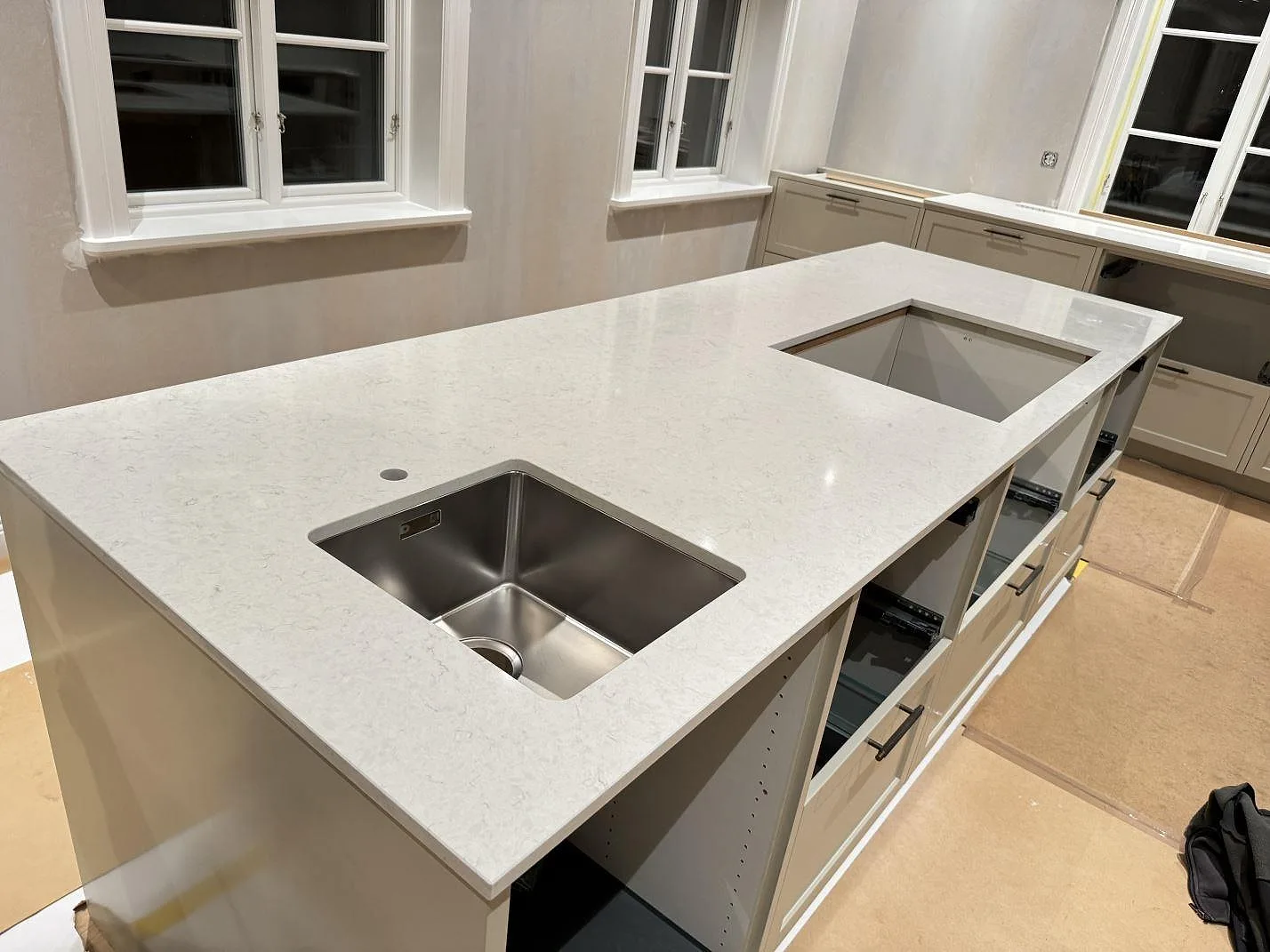 Köksbänkskiva i vit Silestone Snowy Ibiza, polerad, på en frihängande köksö med underlimmad rostfri diskho och urtag för häll i ett kök i Karlshamn.