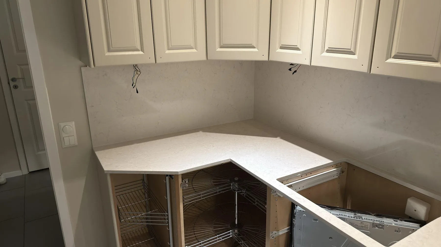 Hörnparti av en köksbänkskiva i vit Silestone Snowy Ibiza med uppvikt stänkskydd i samma sten och hörnkarusell i ett kök i Katrineholm.