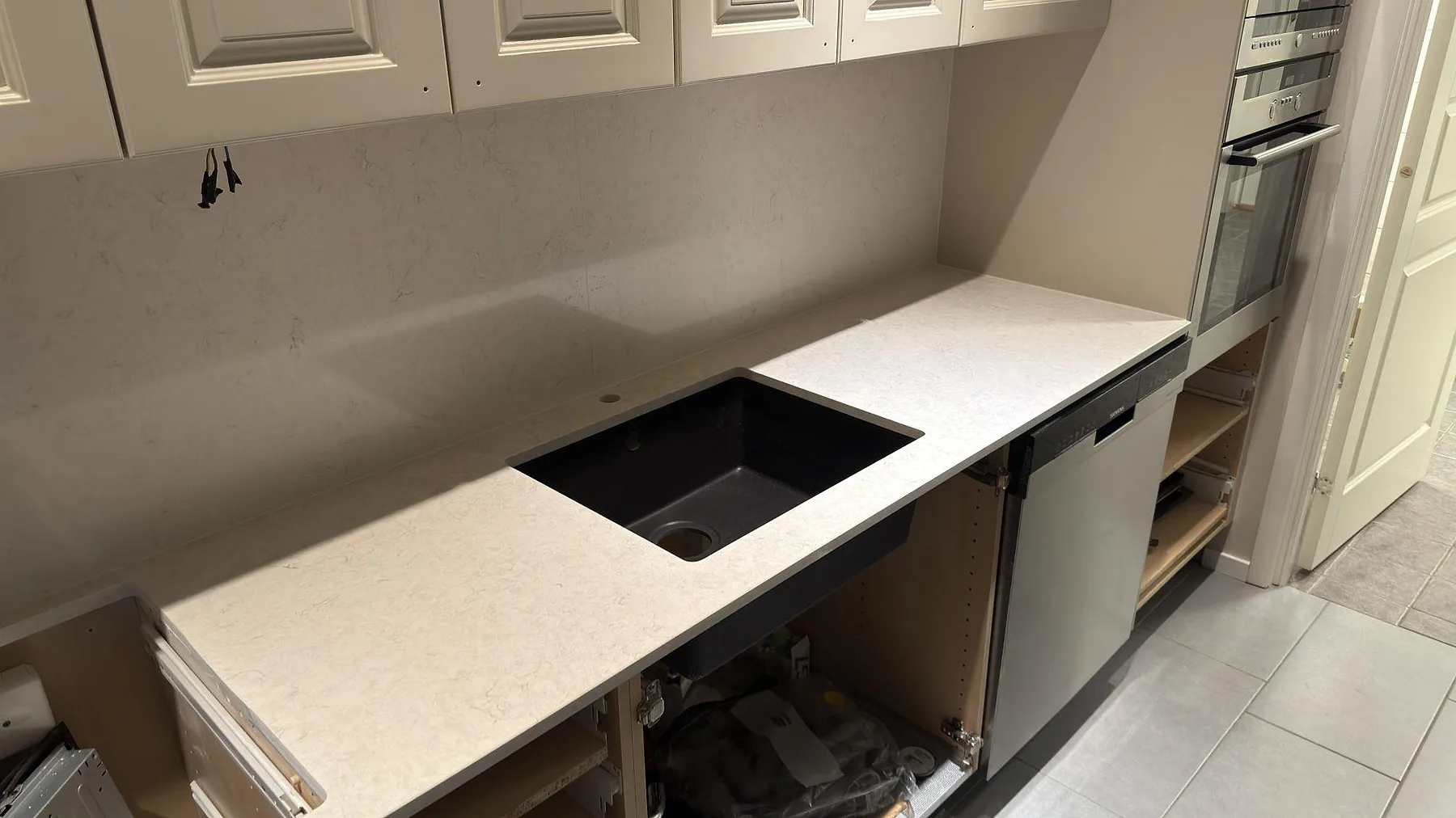 Polerad Silestone Snowy Ibiza bänkskiva med svart underlimmad kompositdiskho och borrat blandarhål samt stänkskydd i samma sten i ett kök i Katrineholm.