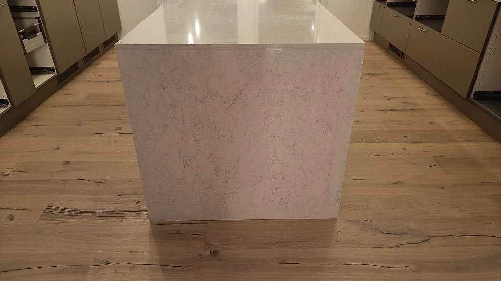 Köksö i polerad Silestone Snowy Ibiza med waterfall-kant ner mot ekgolvet i ett kök i Kivik, med den mjuka grå ådringen tydligt synlig.