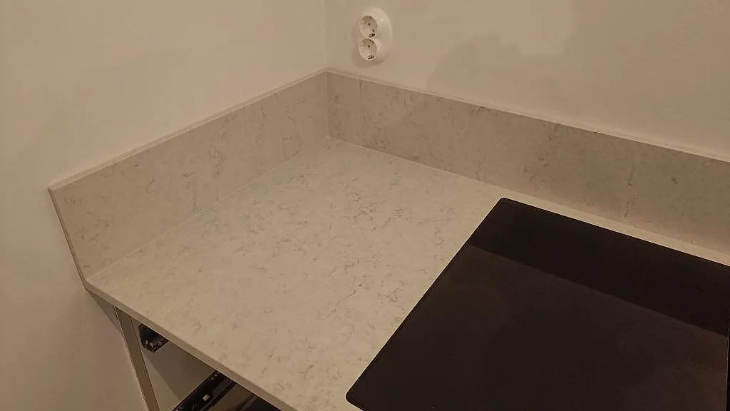 Bänkskiva i Silestone Snowy Ibiza med uppvikt stänkkant i en köksvrå i Kivik, intill en mörk induktionshäll.