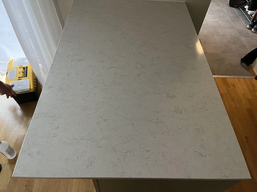 Stor köksö i polerad Silestone Snowy Ibiza med diskret grå ådring i ett kök i Klagshamn.