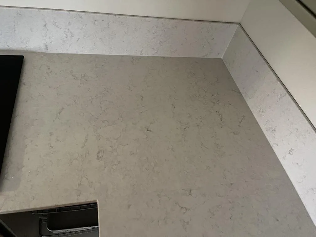 Hörnparti av Silestone Snowy Ibiza bänkskiva med uppvikt stänkkant och infälld häll i ett kök i Klagshamn.