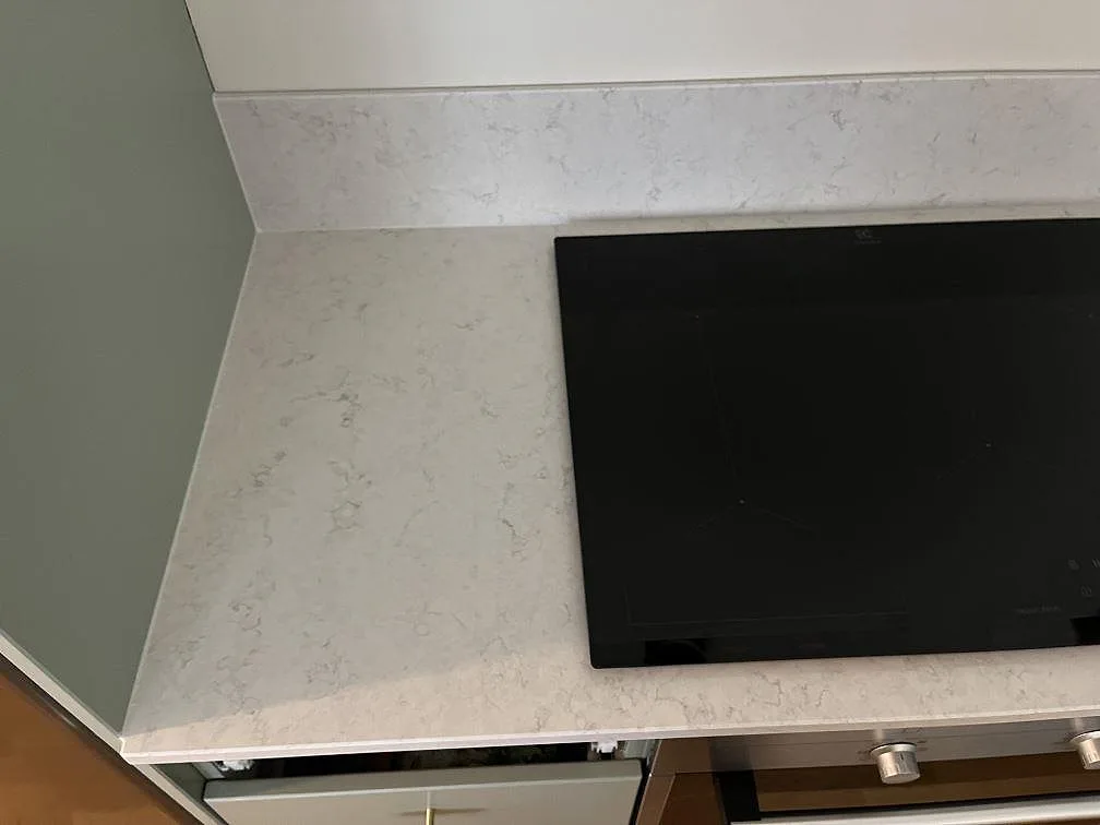 Infälld induktionshäll i polerad Silestone Snowy Ibiza bänkskiva med uppvikt stänkkant i ett kök i Klagshamn.