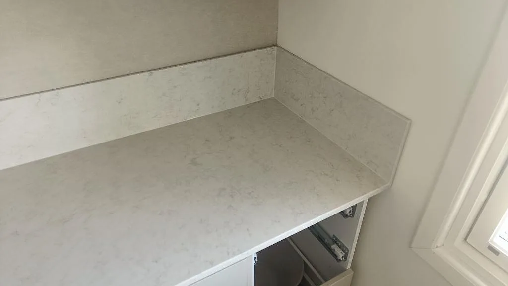 Köksbänkskiva i Silestone Snowy Ibiza med uppvikt stänkskydd i samma sten vid fönster i ett kök i Klippan.