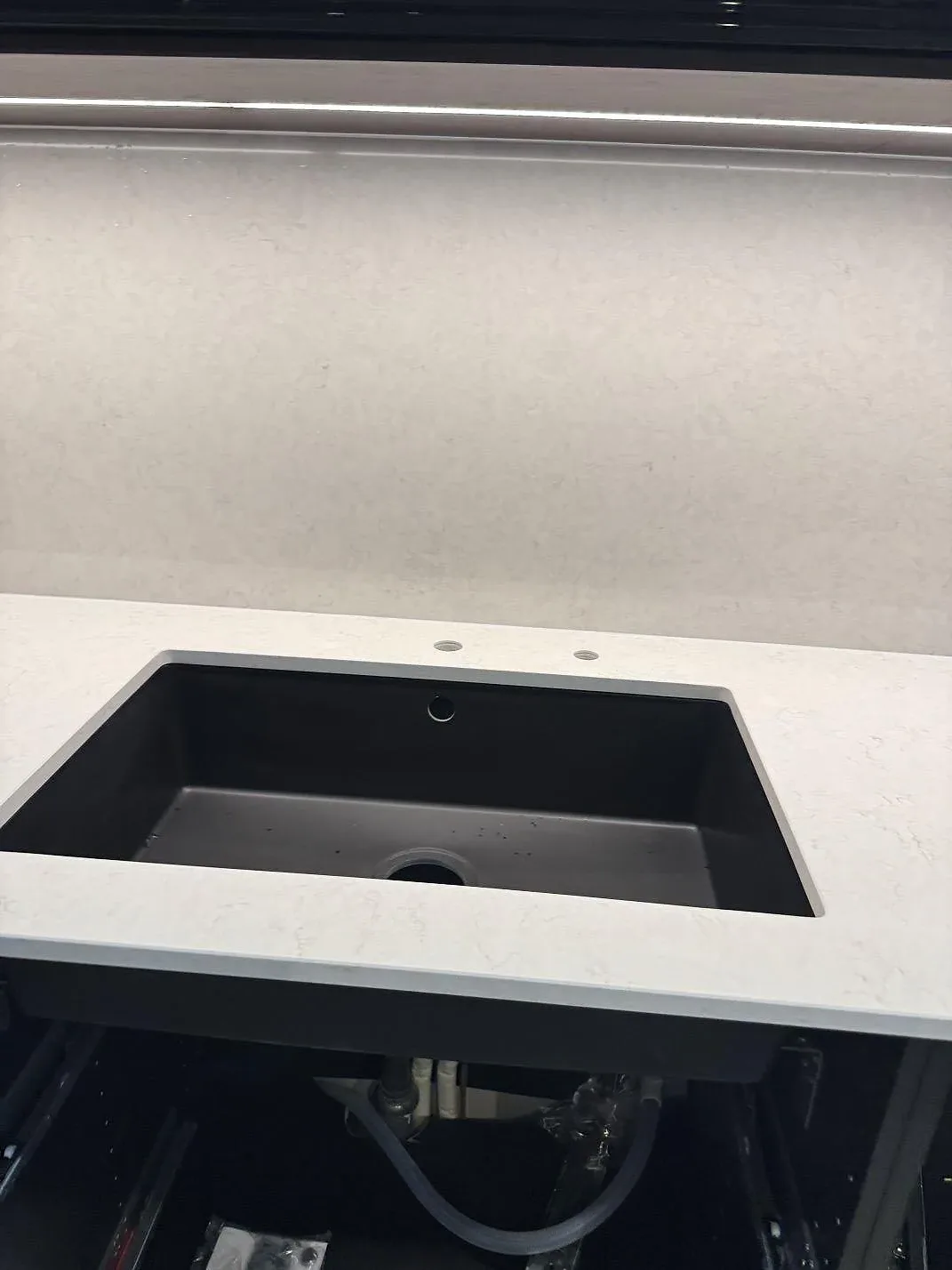 Detalj av den underlimmade svarta kompositdiskhon i den vita köksön av Silestone Snowy Ibiza med plats för blandare i ett kök i Klippan.