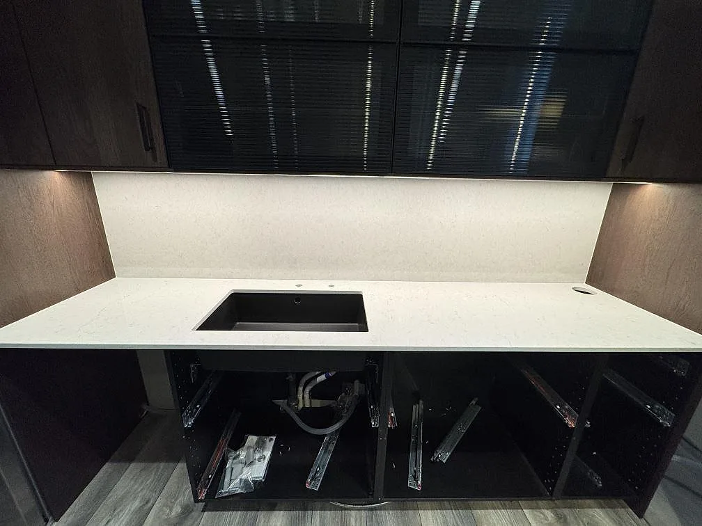 Köksbänkskiva i vit Silestone Snowy Ibiza mot vägg med underlimmad svart kompositdiskho och uppvikt stänkkant under mörka överskåp med räfflat glas i Klippan.
